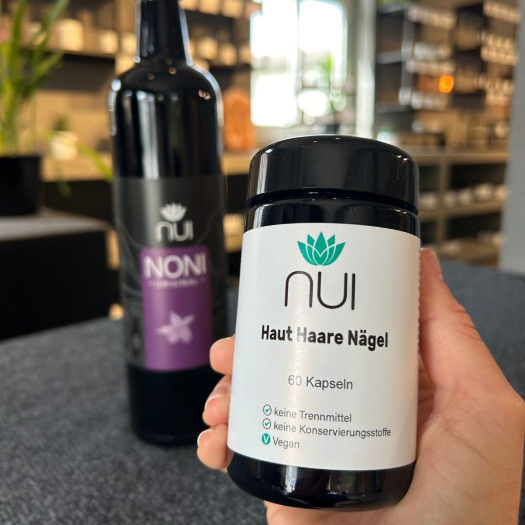 NUI NONI Flasche im Hintergurnd und Haut Haare Nägel Glas in der Hand