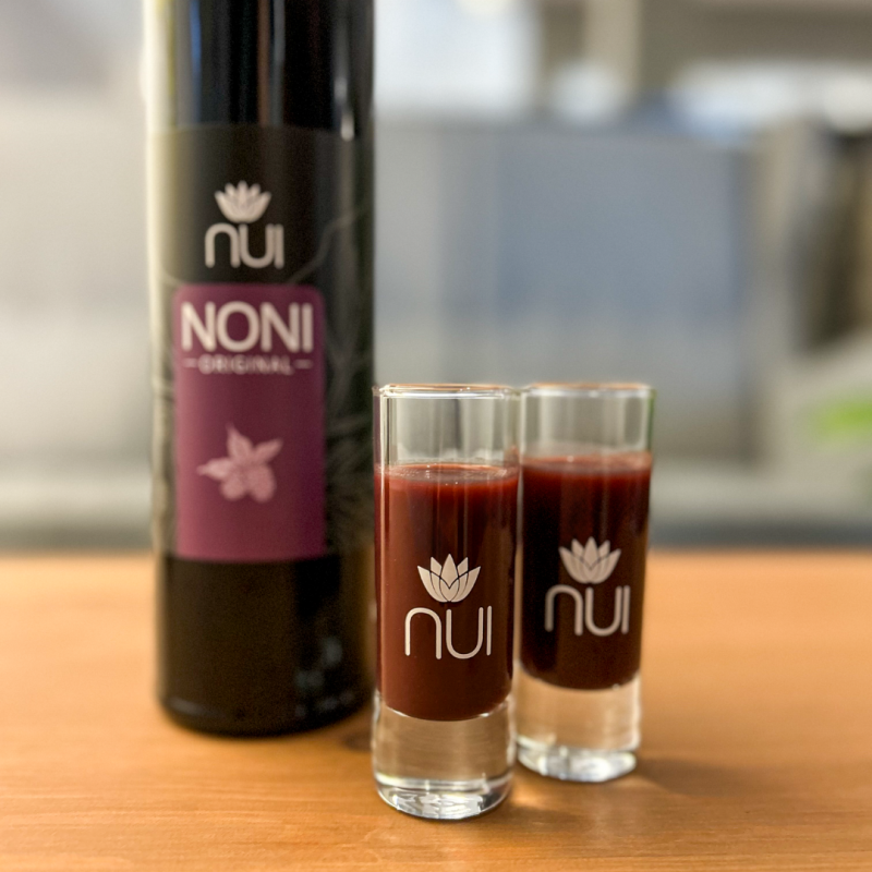 zwei NUI Shotgläser gefüllt mit Noni-Saft im Hintergrund eine NUI NONI Original Flasche