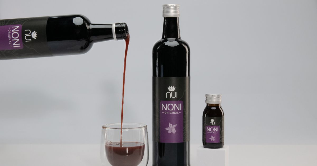 NUI NONI Flasche wird in ein Glas eingeschenkt, daneben steht noch eine Flasche und ein NUI NONI Shot